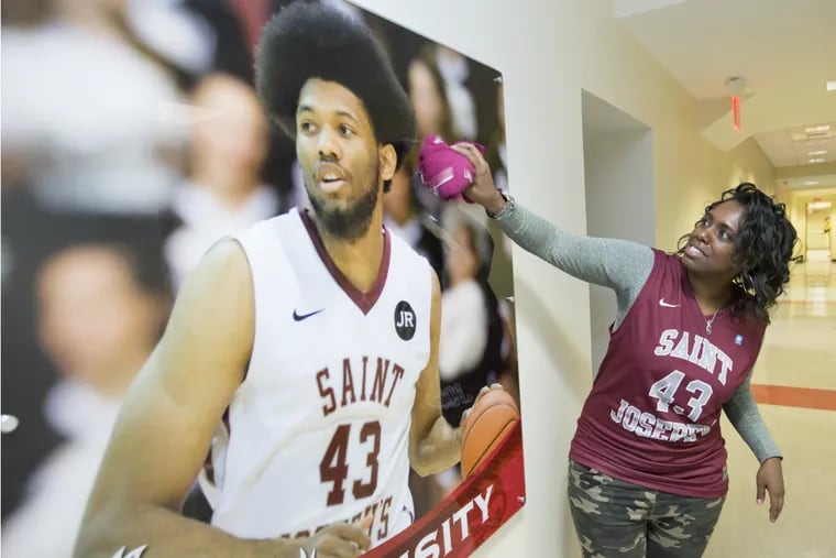 Essence Bembry playfully dusts off poster of  her son, DeAndre', a junior forward at St. Joseph's.