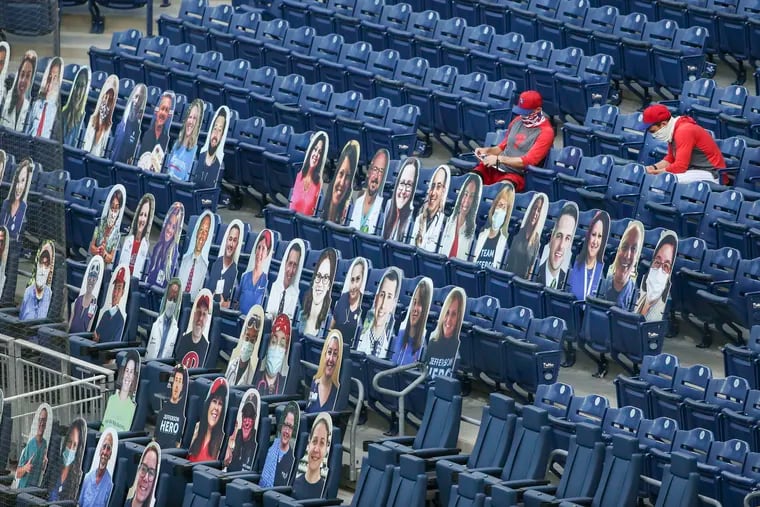 Phillies coaches sit behind likenesses of doctors, nurses and other healthcare workers who have been on the front lines of COVID-19. The cardboard cutouts will be displayed behind home plate during games this weekend.