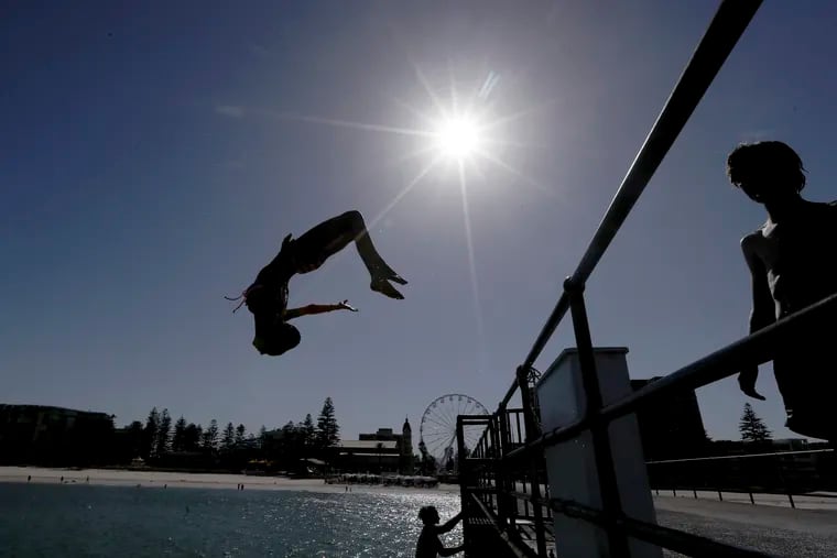 In this Jan. 24, 2019, photo, a beachgoer jumps off a jetty at Glenelg Beach in Adelaide, Australia, as temperatures climb to 45 Celsius (113 ‎Fahrenheit). Australia has sweltered through its hottest month on record in January and the summer of extremes continues with wildfires razing the drought-parched south while expanses of the tropical north are flooded.