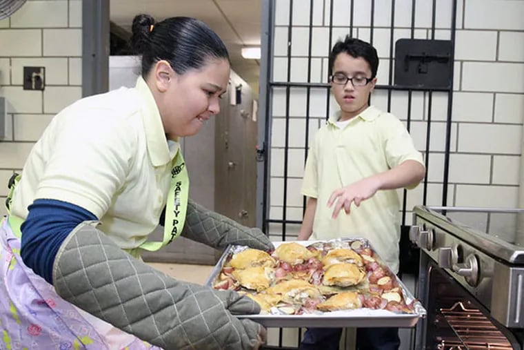 Bianca Perez, left, and Mark Ramirez rotate the pans of chicken, potatoes, and onions in the oven at Bayard Taylor Elementary School in North Philadlephia on Dec. 11, 2013. ( CHARLES FOX / Staff Photographer )