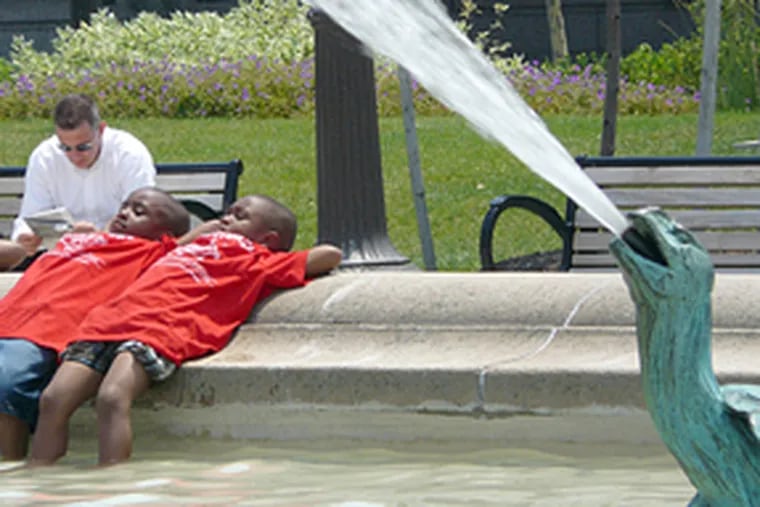 Mugahib Jamaddlin, left, and Nashyne Dawkins lounge on the side of Swann Fountain on the Benjamin Franklin Parkway in Center City. The children, from the R.W. Brown Community Center in North Philadelphia, were on a day trip to the Academy of Natural Sciences and detoured across the Parkway to cool off at the fountain.