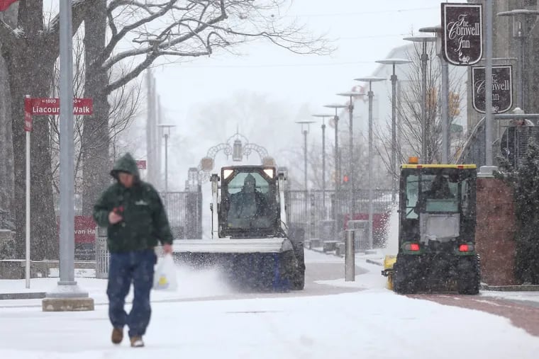 Workers clear snow from walkways as snow falls on the Temple University campus.