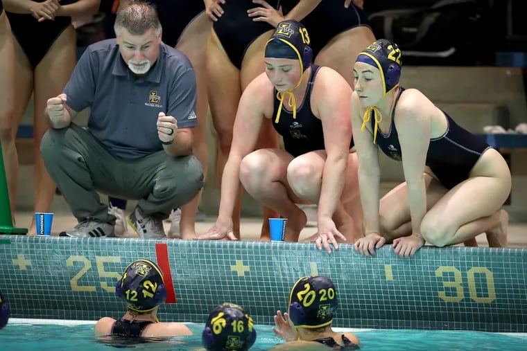 La Salle head coach Tom Hyham (left) talks with his team during a timeout as they play Marist in a water polo match at La Salle University in Philadelphia, Pa. on Sunday, April 3, 2022. Kalista Hyham (right), his daughter, and teammate Sophie Appler (center) listen on the pool deck.