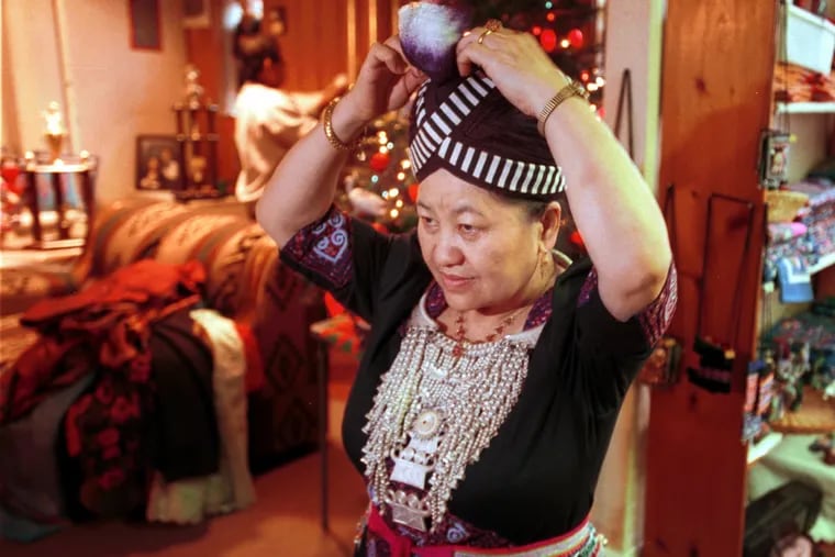 Pang Xiong Sirirathasuk Sikoun, in a 2000 photograph, uses a mirror to adjust her traditional Hmong outfit.