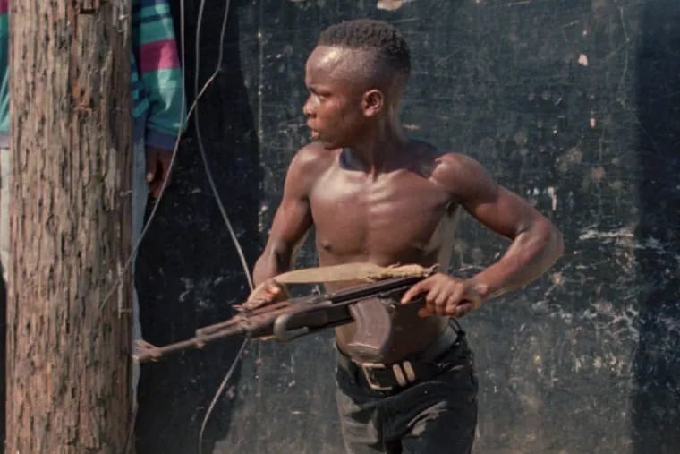 A teenage fighter with the National Patriotic Front of Liberia (NPFL) charges forward in downtown Monrovia, Liberia, on May 10, 1996.