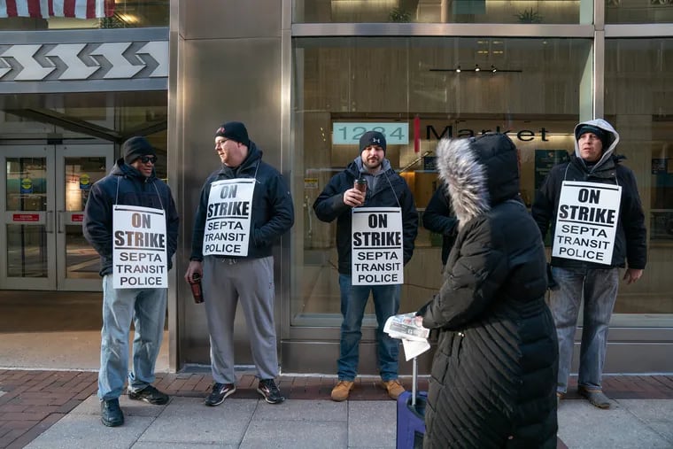 A bundled up pedestrian walks past SEPTAÕs transit police on strike outside SEPTA Headquarters on the 1200 block of Market Street, Thursday, March 7, 2019, in Philadelphia. The men photographed preferred not to give their names.