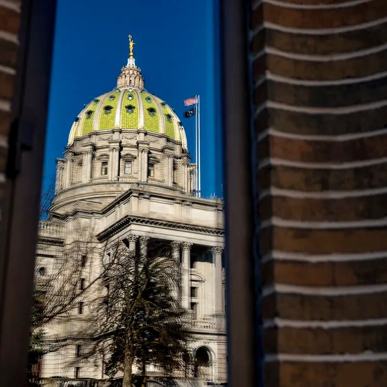 The Pennsylvania state Capitol building is reflected in the windows of an office building on North Third Street in Harrisburg. Vouchers like those being considered by the legislature have led to some of the largest academic declines in the history of education research, writes Joshua M. Cowen.