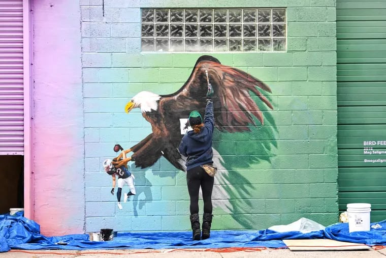 Artist Lizzie Kripke, helps paint “BIRD FEED” on the walls outside of Meg Saligman’s studio in Bella Vista.
