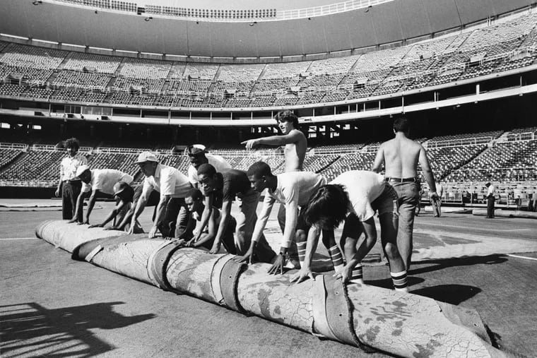 Grounds crew take up the AstroTurf at third base in Veterans Stadium to convert the field from football to baseball on Aug. 1, 1981.