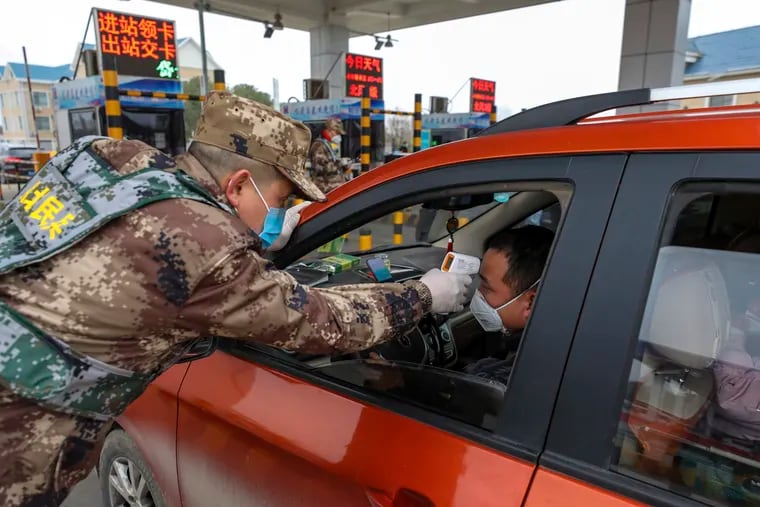 A militia member uses a digital thermometer to take a driver's temperature at a checkpoint at a highway toll gate in Wuhan in central China's Hubei Province on Thursday. China closed off a city of more than 11 million people Thursday in an unprecedented effort to try to contain a deadly new viral illness.