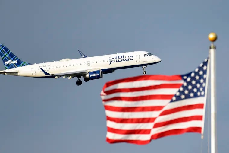 FILE - In this Sept. 21, 2018, file photo, a plane flies past the American flag in Washington. JetBlue plans to join bigger rivals in offering flights between the U.S. and Europe, starting with London in 2021.
