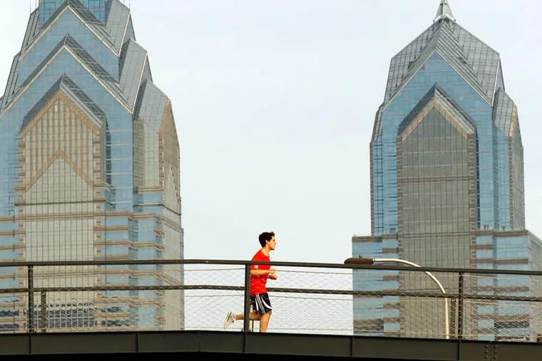 File: A jogger runs on the entrance to the Walnut Street Bridge with One and Two Liberty Place behind him.