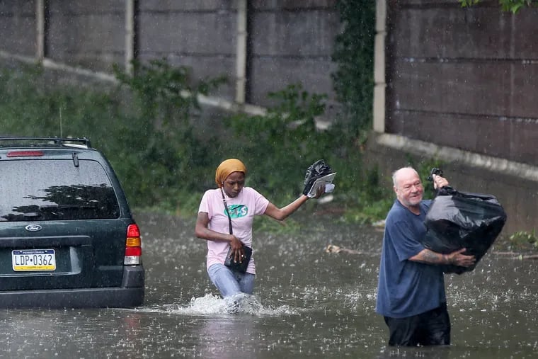 Bob Dugon helps his friend Kiearra Price retrieve belongings from her car after it was caught in floodwaters on West Hunting Park Avenue at Ridge Avenue in North Philadelphia in July when Tropical Storm Fay wrung out heavy rains over the region.