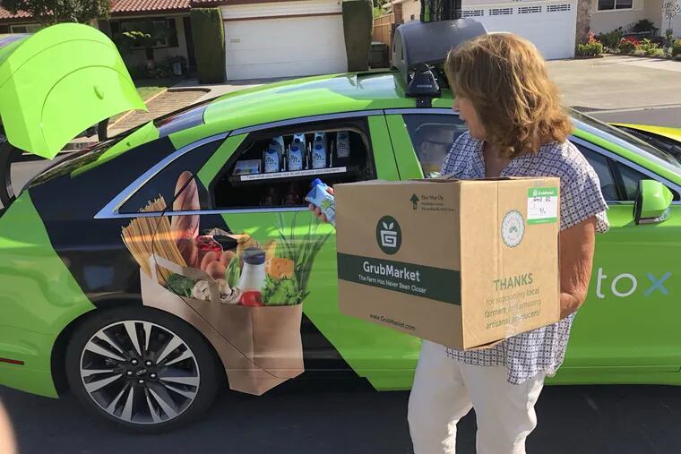 A customer grabs part of her delivery from the backseat window of a self-driving car in San Jose, Calif.  While the services are likely coming, developers aren't yet ready to change designs to accommodate them.