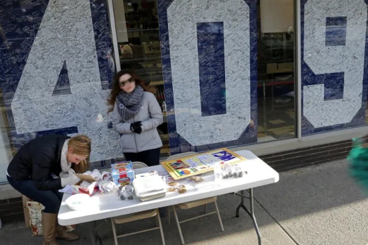 Penn State students Jackie Jones (left) and Jacqueline
Browne staff a bake sale table in front of the Penn State Student Bookstore that displays Joe Paterno's win total.