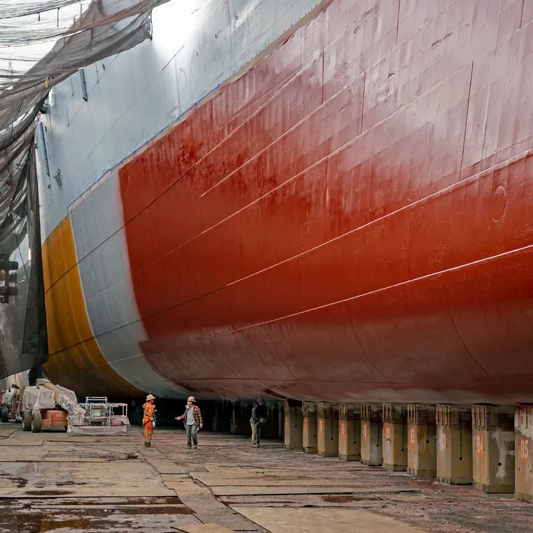 Workers are dwarfed by the hull of the Battleship New Jersey at Philadelphia Ship Repair. The ship is berthed in Dock No. 3, from which it was launched on Dec. 7, 1942.