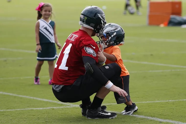 Eagles quarterback Carson Wentz lets tight end Trey Burton’s son, Jaxon, 2, tackle him after practice on Friday.