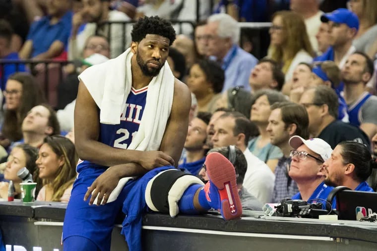 Joel Embiid rests at the scorers table with a heating pad on his knee during the Sixers' Game 1 loss to the Nets.