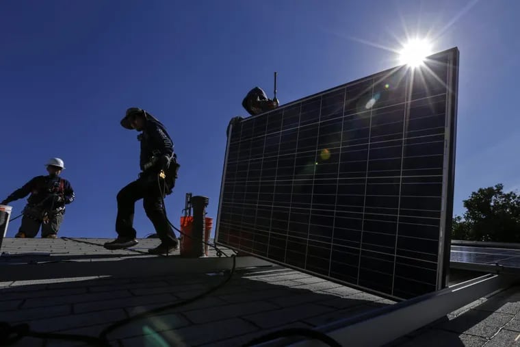 Workers install solar panels on a roof.
