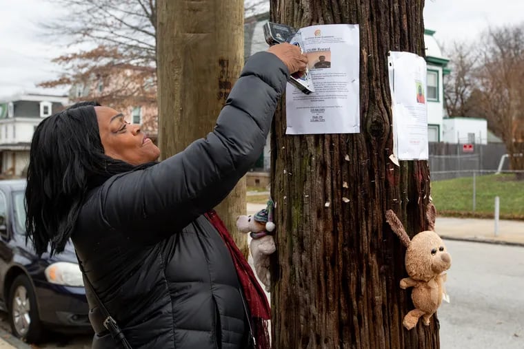 Yullio Robbins, of West Philadelphia, hangs a sign to help find answers to her son's murder in Germantown in 2018. James Walke III was murdered in 2016. His case remains unsolved.