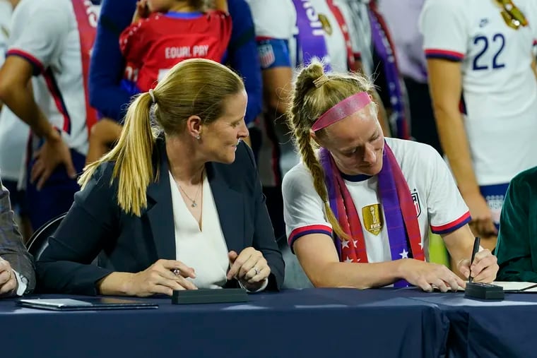 U.S. Soccer Federation president Cindy Parlow Cone (left) watches current women's national team captain Becky Sauerbrunn (right) ceremonially sign the program's new collective bargaining agreement.