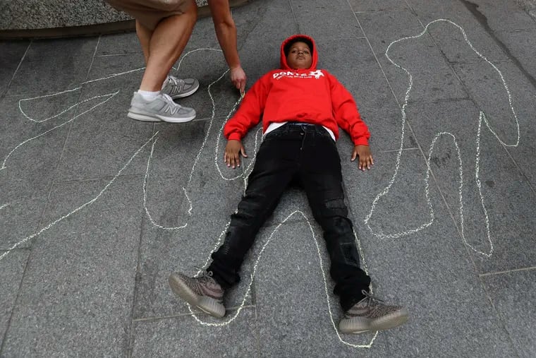 Cordell Harrell, 11, lays down on the sidewalk as Max Milkman draws a chalk outline at a "die-in" at City Hall Thursday. Students laid motionless to dramatize the loss of life from the city's gun violence epidemic.