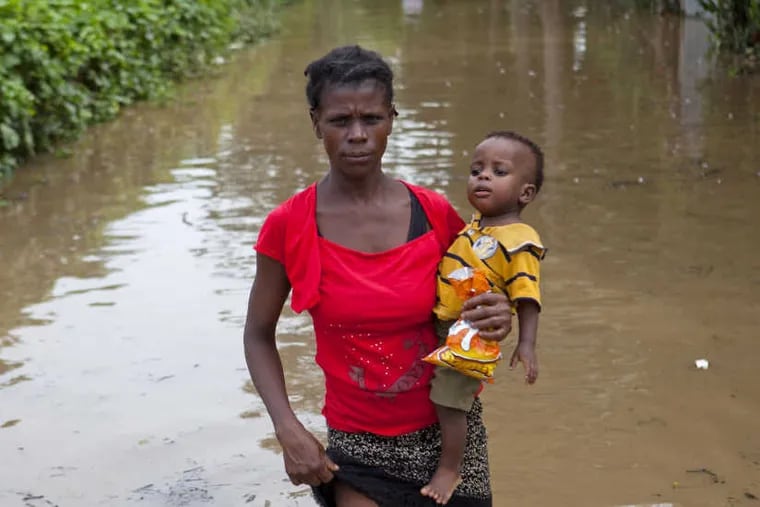 A woman carries her little son from her home which was flooded by rains brought on by Hurricane Irma, in Fort-Liberte, Haiti, Friday Sept. 8, 2017. Irma rolled past the Dominican Republic and Haiti and battered the Turks and Caicos Islands early Friday with waves as high as 20 feet.