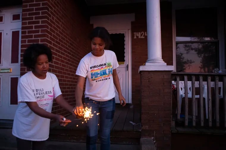 Veronica Hampton (left) passes Jayla Johnson a sparkler in North Philadelphia in May. Johnson and a group of kids took turns playing with the sparklers.
