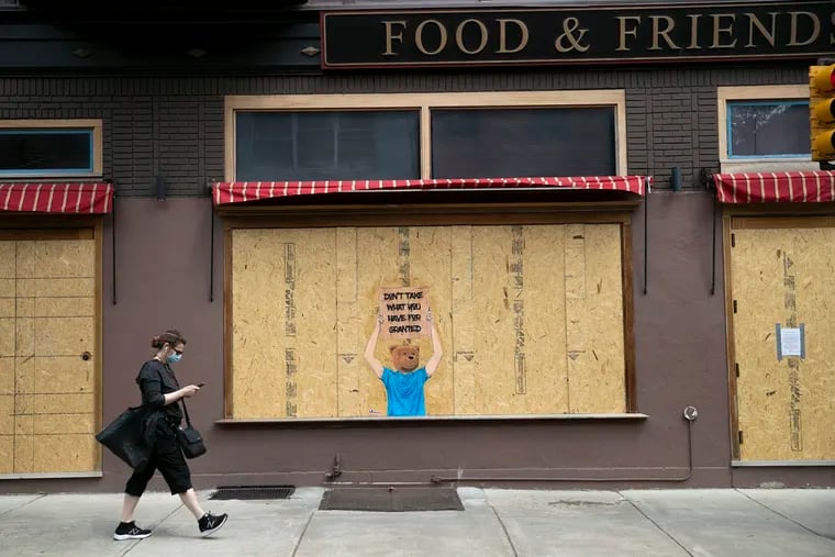 A masked pedestrian walks by a boarded up Food & Friends with a message that says "Don't Take What You Have For Granted" in Center City Philadelphia on Wednesday, April 29, 2020. All nonessential businesses are closed due to the coronavirus (COVID-19). Restaurants are takeout or delivery only.