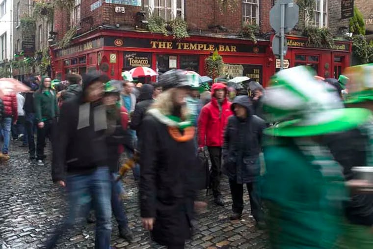 Pedestrians carrying umbrellas and wearing St. Patrick's day hats and scarves move past the Temple Bar public house in Dublin, Ireland, on Sunday, March 17, 2013. Ireland’s renewed competiveness makes it a beacon for the U.S. companies such as EBay, Google Inc. and Facebook Inc., which have expanded their operations in the country over the past two years. Photographer: Simon Dawson/Bloomberg