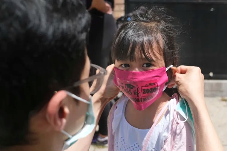 Olivia Chan's father helps her with a new mask she received during a graduation ceremony for her Pre-K class in front of Bradford School in Jersey City. As the Trump administration pushes to force schools to resume in-person education, public health experts say precautions and adaptations must be tailored by local officials and parents.