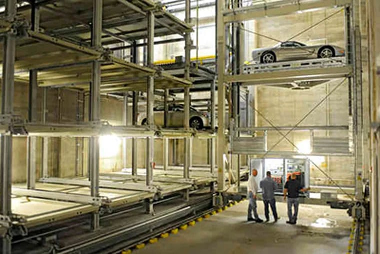 Workmen adjust the automated parking system inside the garage at 1706 Rittenhouse Square Street, with one car on a pallet that deposits and retrieves the cars. (Clem Murray / Staff Photographer)