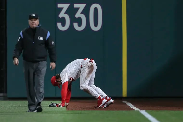 Phillies' right fielder Bryce Harper stretches after hitting the wall catching Brewers' Keston Hiura foul ball during the 6th  inning at Citizens Bank Park in Philadelphia, Tuesday, May 14, 2019 Umpire Mike Everitt is at left.  Brewers beat the Phillies 6-1.