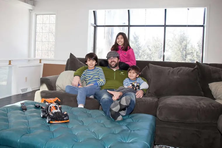 Stephen O'Sullivan and his three children lounge in their reinvented TV room, with furniture that can survive many play sessions. Emily Cohen / For the Philadelphia Inquirer