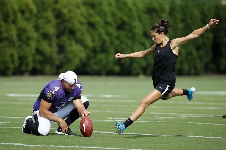 Baltimore Ravens' Sam Koch holds the ball for United States soccer player Carli Lloyd as she attempts to kick a field goal after the Philadelphia Eagles and the Baltimore Ravens held a joint NFL football practice in August. Lloyd's kicking is featured in a Super Bowl ad.