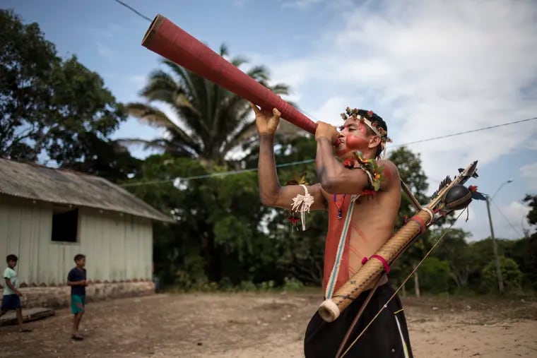 In this Sept. 3, 2019 photo, a man plays a horn during a meeting of Tembé tribes in Tekohaw indigenous reserve, Para state, Brazil. Under a thatch-roof shelter in the Amazon rainforest, warriors wielding bows and arrows, elderly chieftains in face paint and nursing mothers gathered to debate a plan that some hope will hold at bay the loggers and other invaders threatening the tribes of the Tembe.