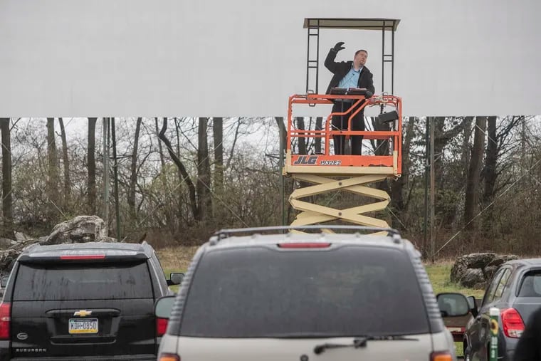 With the movie screen behind him, Pastor Barry Van Hussey of the Christian Life Community Church in Newville, Pa, preaches perched atop a scissor boom, over the tops of the cars gathered in the Cumberland Drive-In Theatre on Sunday.