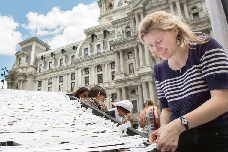 Sofia Seidel, an assistant at Meg Saligman Studios, helps participants with a public art exhibit on the grounds of City Hall. Rumination and prayer are part of the work's aim.