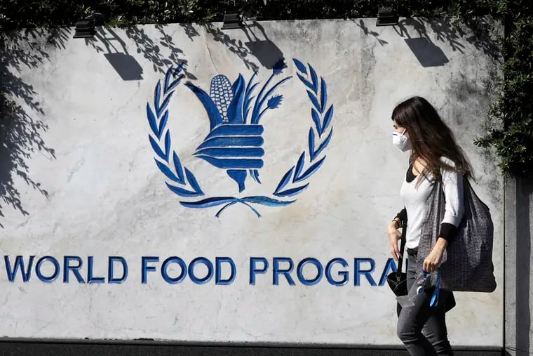 A woman wearing a face mask walks past a sign at the entrance of the United Nations World Food Program (WFP), in Rome on Oct. 9, 2020, after the WFP won the 2020 Nobel Peace Prize.