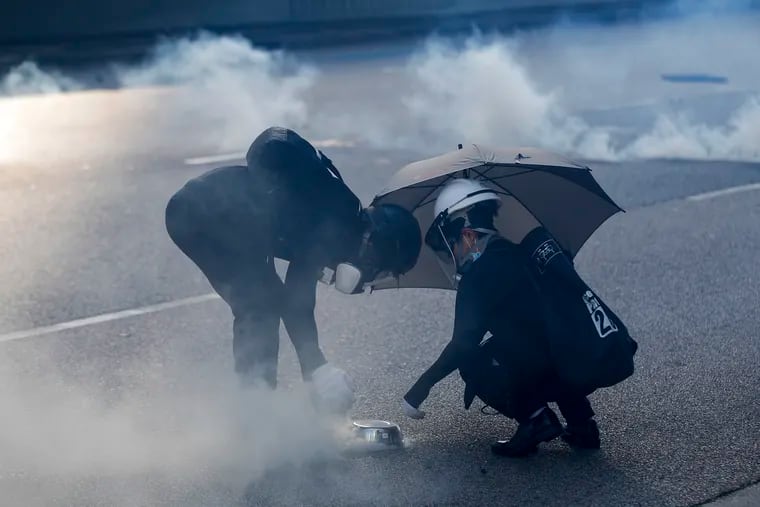 Protester uses a plate to cover a tear gas canister fired by riot police as they face off near the Legislative Council building and the Central Government building in Hong Kong, Monday, Aug. 5, 2019. (AP Photo/Vincent Thian)