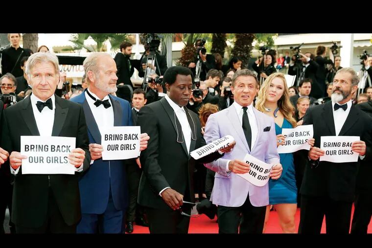 The cast of The Expendables 3, from left, Kelsey Grammer, Wesley Snipes, Sylvester Stallone, Ronda Rousey and Mel Gibson hold up banners reading, "Bring back our girls", part of a campaign calling for the release of nearly 300 abducted Nigerian schoolgirls being held by Nigerian Islamic extremist group Boko Haram, as they arrive for the screening of The Homesman at the 67th international film festival, Cannes, southern France, Sunday, May 18, 2014. (AP Photo/Alastair Grant)