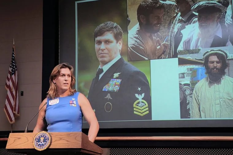 Kristen Beck, who served as a Navy Seal during 20 years in the military, stands before pictures of herself in the military while speaking at the FBI Criminal Justice Information Services Division in 2014.