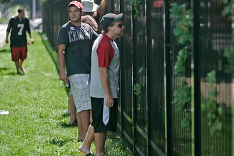 Anthony Carugno (right) Graham Kington (looking back) try to catch a glimpse of Michael Vick through the fence at the NovaCare Center. Some angry fans have sworn off the Eagles.     (Michael Bryant / Staff Photographer)