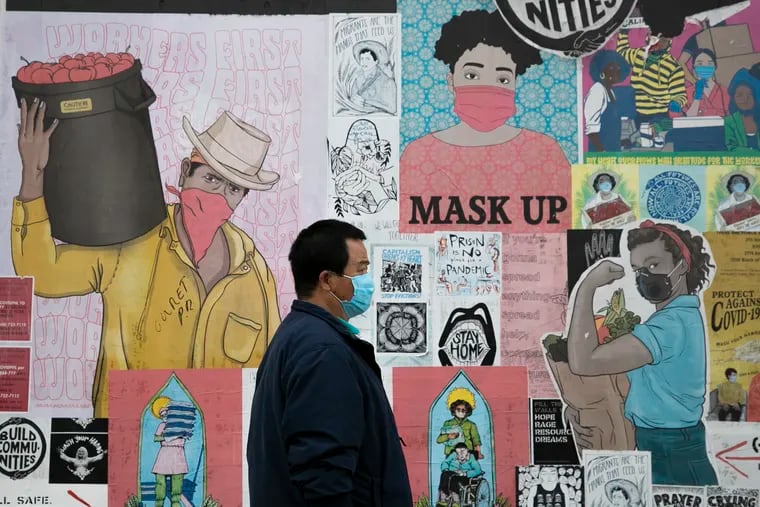 A pedestrian walks past street murals encouraging Philadelphians to wear masks and keep six feet apart at Ridge Avenue and Spring Garden Street.