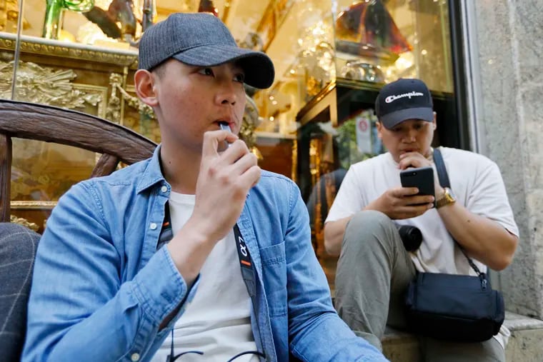 In this Monday, June 17, 2019, photo, Joshua Ni, 24, and Fritz Ramirez, 23, vape from electronic cigarettes in San Francisco. San Francisco supervisors are considering whether to move the city toward becoming the first in the United States to ban all sales of electronic cigarettes in an effort to crack down on youth vaping. The plan would ban the sale and distribution of e-cigarettes, as well as prohibit e-cigarette manufacturing on city property.