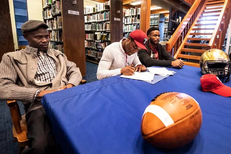 Penn Charter's Edward Saydee, center, in company of his father, Tarlue Saydee, left, and Eugene Saydee, brother, signs national letter of intent to play football at Temple at Penn Charter School in Philadelphia, Pa. Wednesday, December 19, 2018. JOSE F. MORENO / Staff Photographer