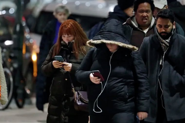 People engaged with their cell phones wait to cross Broad St at Market St. during the evening rush hour in Philadelphia on December 4, 2019.