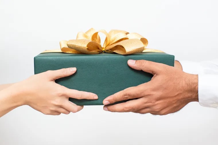 Close-up of couple holding packaged Christmas present together. Woman passing gift to boyfriend while congratulating him with New Year. Christmas gift-giving concept