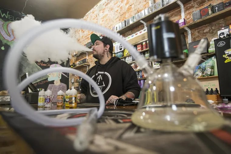 Myk Londino, manager of Vape O2 in Philadelphia, uses an e-cigarette behind the shop counter. The shop is one of many affected by Pennsylvania’s vape tax.