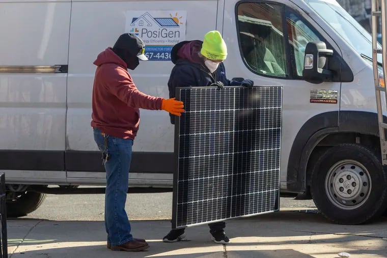 PosiGen employees, Eric Cwiklinski (left) and Tim Miller, prepare to install solar panels on the home of Aminata Sandra Calhoun in Philadelphia. Calhoun is a participant in the Philadelphia Energy Authority's new solar lease program.